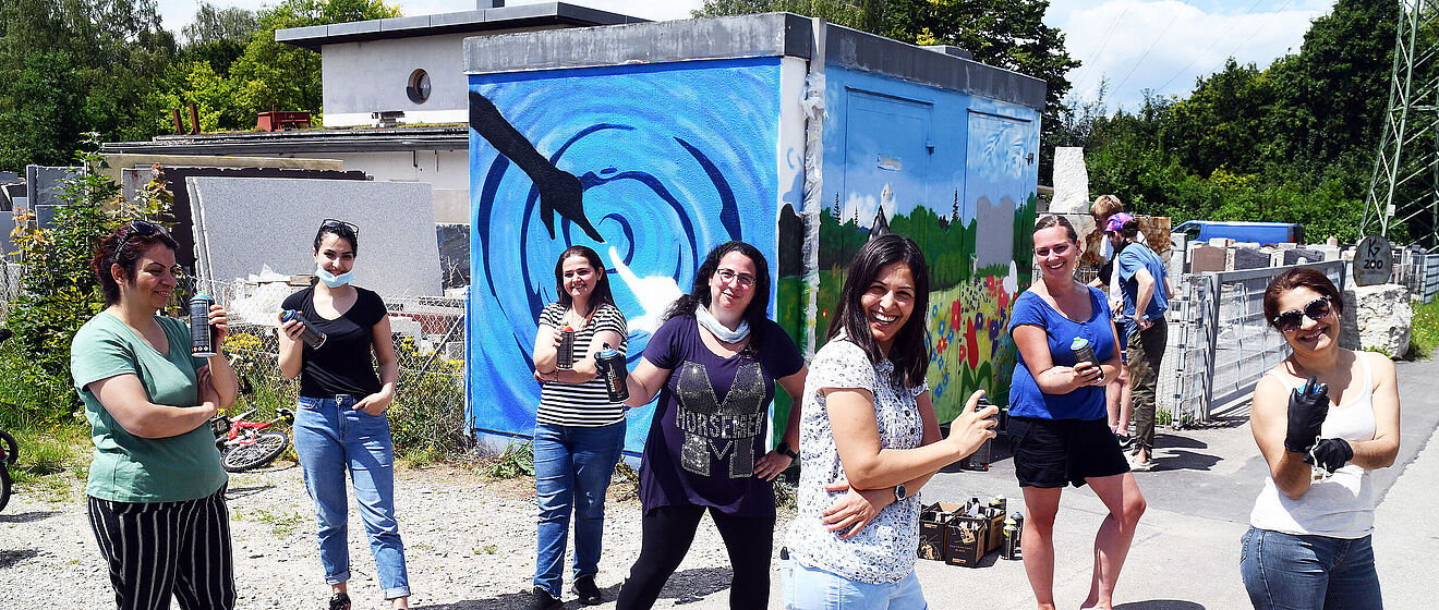 Eine Gruppe von Personen mit Spraydosen in der Hand, stehen vor einem bunt bemalten Gebäude