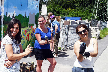 Eine Gruppe von Personen mit Spraydosen in der Hand, stehen vor einem bunt bemalten Gebäude