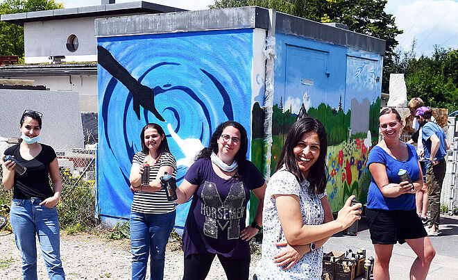 Eine Gruppe von Personen mit Spraydosen in der Hand, stehen vor einem bunt bemalten Gebäude