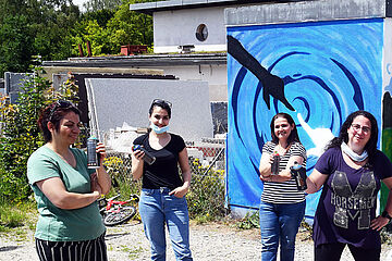 Eine Gruppe von Personen mit Spraydosen in der Hand, stehen vor einem bunt bemalten Gebäude