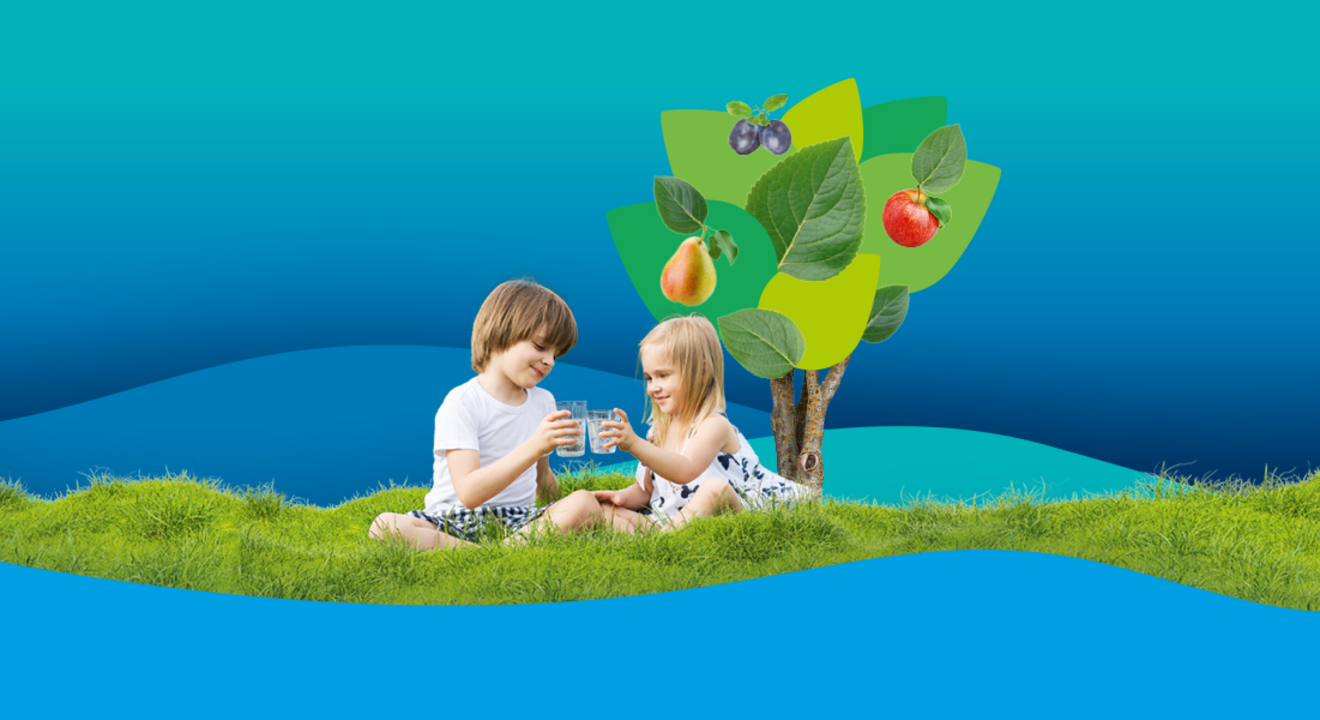 Zwei Kinder sitzen lächelnd mit einem Glas Wasser auf einer grünen Wiese. Im Hintergrund ist ein Baum mit Äpfeln