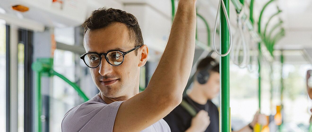 Mann mit Brille der sich an der oberen Stange eines öffentlichen Verkehrsmittels festhält. Mit Link zum öffnen einen Pop-Ups mit Informationen zum Mobil-Abo