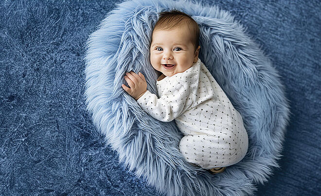 Ein lachendes Baby liegt auf einem grauen Wollkissen und schaut in die Kamera. Weiterverlinkung auf swa Energiewendeseite