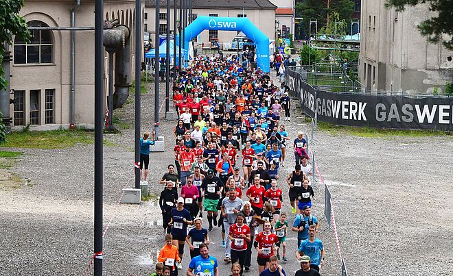 Läufer mit swa Trikot laufen beim swa Spendenlauf. Im Hintergrund ist das Ziel mit swa Branding