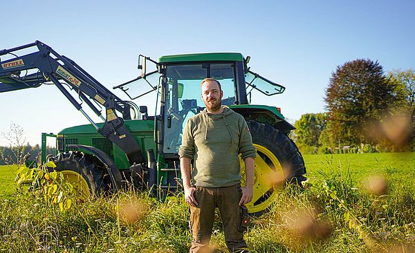 Benedikt Brem vor einem Traktor auf einem Feld. 