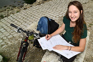 Mädchen bearbeitet Aufgaben, neben ihr steht ein Fahrrad. - Beim anklicken wird das Bild vergrößert.