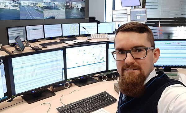 Ein Selfie von einem Mann, welcher vor mehreren Monitoren sitzt.