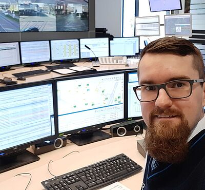 Ein Selfie von einem Mann, welcher vor mehreren Monitoren sitzt.