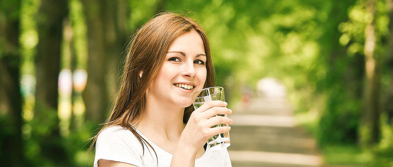 Frau im Wald mit einem Glas Wasser in der Hand. 