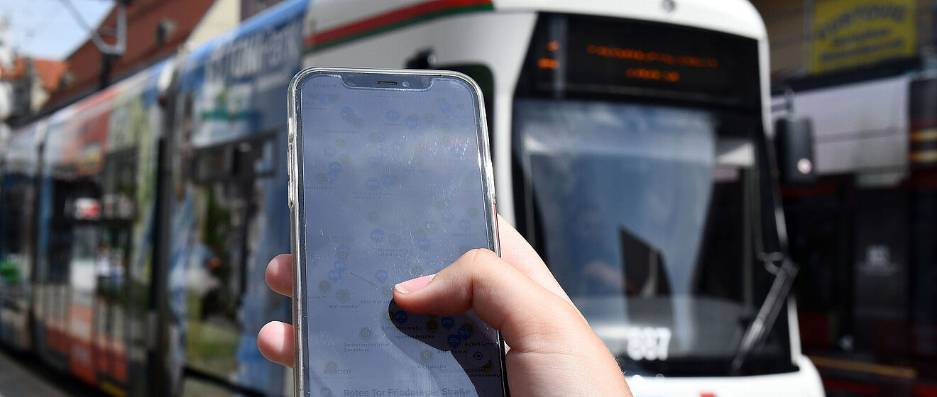 Nahaufnahme eines Handyscreens, auf dem die swa MobilApp gezeigt wird. Im Hintergrund eine swa Tram.
