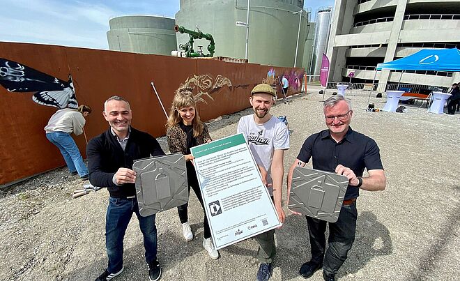 Vier Personen halten Auszeichnungen in der Hand. Im Hintergrund sprühen Leute Graffiti auf eine Schwabenwand. Weiterverlinkung auf eine Schwabenwand auf dem Gaswerkgelände Newsartikel