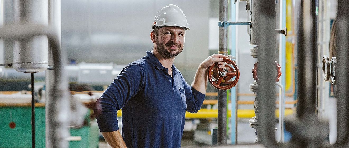 Mann mit Helm und swa Pullover hält ein Ventil in einem Heizkraftwerk