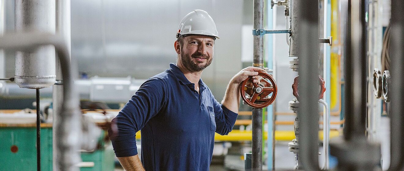 Mann mit Helm und swa Pullover hält ein Ventil in einem Heizkraftwerk