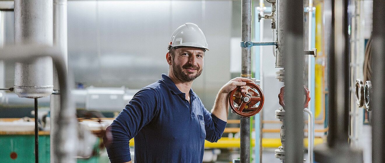Mann mit Helm und swa Pullover hält ein Ventil in einem Heizkraftwerk