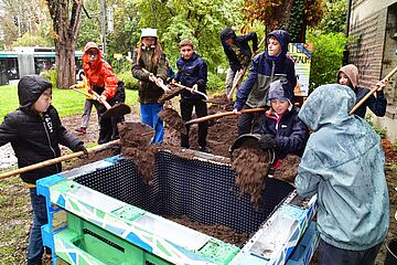 Kinder schaufeln Erde in ein Hochbeet aus Europaletten.
