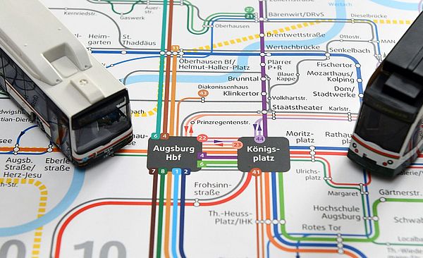 Ein Augsburger Nahverkehrsnetzplan, auf dem zwei Modellstraßenbahnen platziert sind.