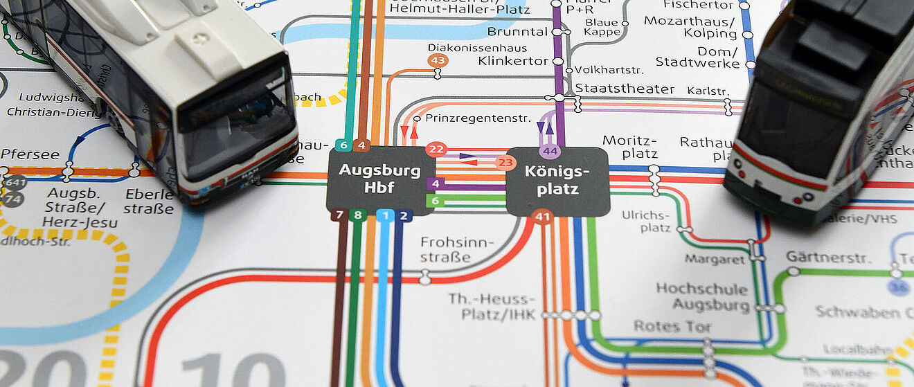 Ein Augsburger Nahverkehrsnetzplan, auf dem zwei Modellstraßenbahnen platziert sind.