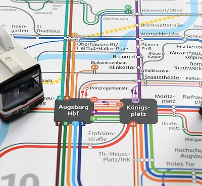 Ein Augsburger Nahverkehrsnetzplan, auf dem zwei Modellstraßenbahnen platziert sind.