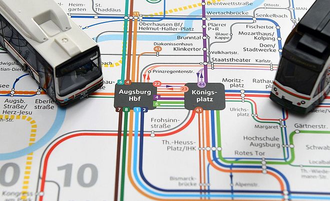 Ein Augsburger Nahverkehrsnetzplan, auf dem zwei Modellstraßenbahnen platziert sind.
