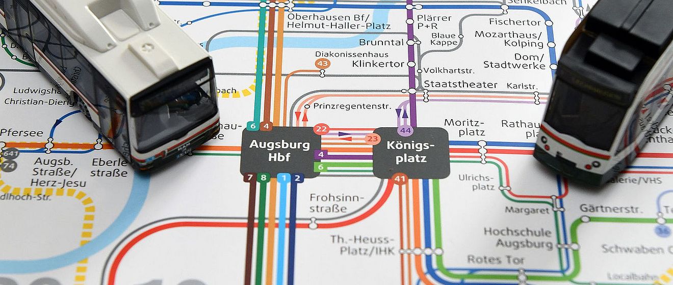 Ein Augsburger Nahverkehrsnetzplan, auf dem zwei Modellstraßenbahnen platziert sind.