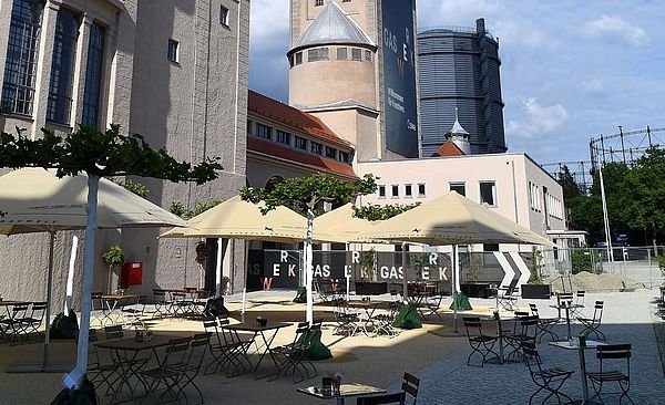 Gaswerksareal mit Sitzmöglichkeiten, Tischen und Sonnenschirmen
