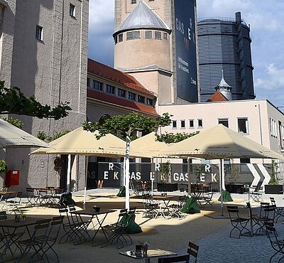 Gaswerksareal mit Sitzmöglichkeiten, Tischen und Sonnenschirmen