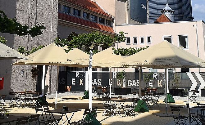Gaswerksareal mit Sitzmöglichkeiten, Tischen und Sonnenschirmen. Weiterverlinkung auf Gaswerksareal Newsartikel