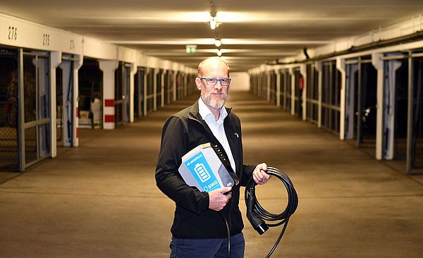 Ein Mann steht in einer Tiefgarage und hält eine eLadebox von den swa als auch ein Ladekabel in der Hand.