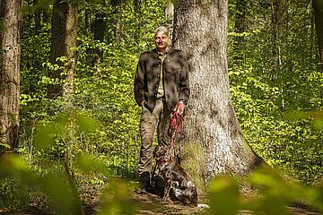 Förster steht mit seinem Hund im Wald. - Ein Klick auf das Bild führt zur vergrößerten Fotoansicht.