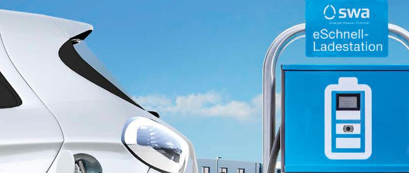 Renault Zoe an E-Ladesäule angeschlossen. Im Hintergrund ist ein Wohnblock mit parkenden Autos.