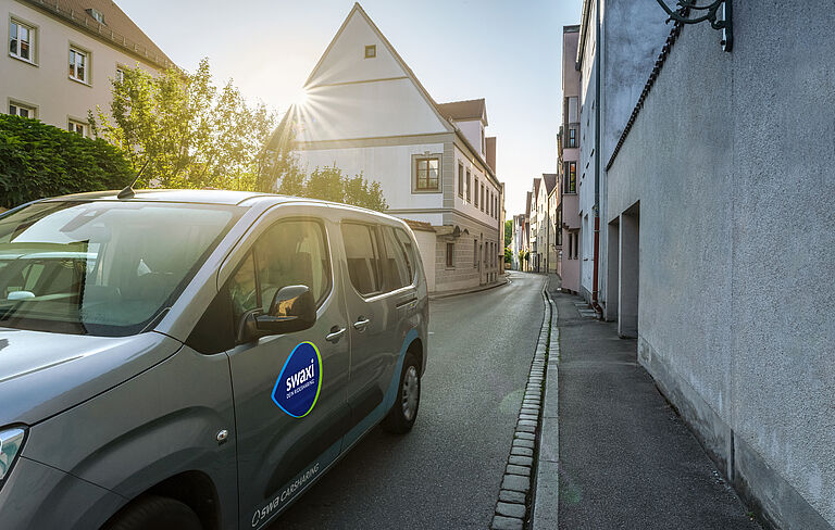 Ridesharing Auto "swaxi" mit Wohnblöcken im Hintergrund