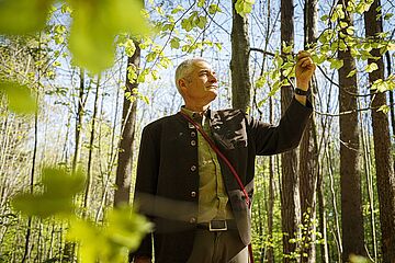 Förster steht im Wald und betrachtet Blätter. - Ein Klick auf das Bild führt zur vergrößerten Fotoansicht.