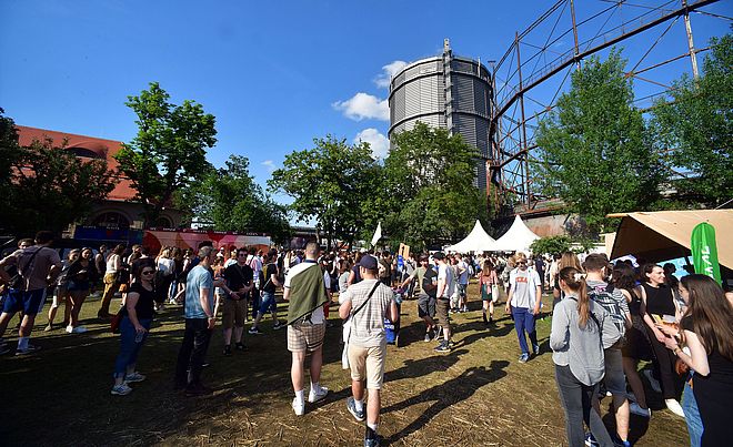 Menschen laufen auf dem Gaswerksgelände. Im Hintergrund ist der Gaskessel. Weiterverlinkung auf Modular 2022 Newsartikel