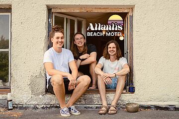 Drei Männer sitzen lachend an einem Fenster vom Atlantis Beach Motel. Ein Klick auf das Bild sorgt für eine Großansicht