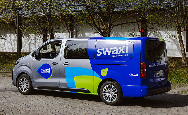 swaxi Transporter mit swaxi Branding an den Seite steht auf einem Parkplatz.
