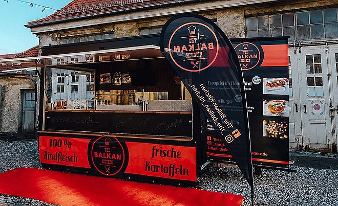Frontansicht auf Balkan Kitchen mit Bannern und roten Teppich auf dem Boden. Weiterverlinkung auf The Balkan Kitchen Newsartikel