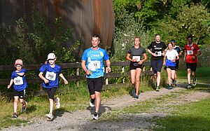 Mann mit swa Trikot läuft beim swa Spendenlauf im Wald. Links sind Zwei Kinder und im Hintergrund andere Läufer