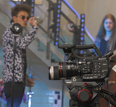 Filmkamera. Im Hintergrund sind Leute mit Instrumenten.