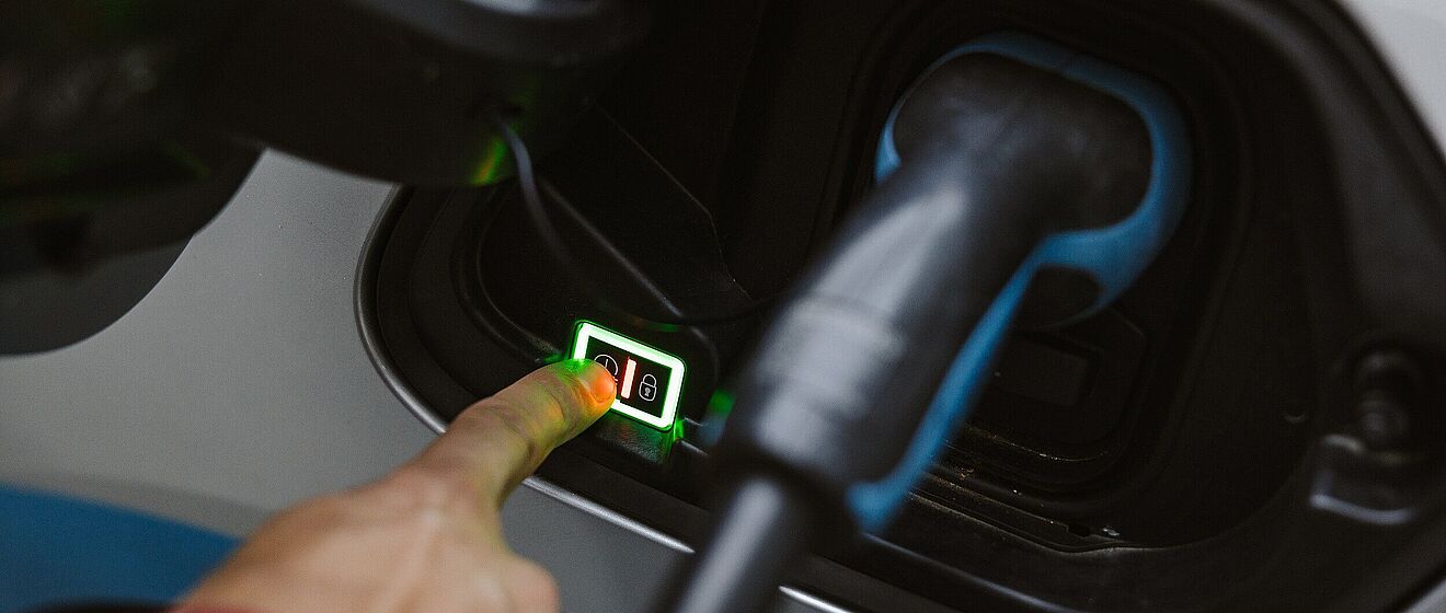 Auto ist an eine eLadesäule gekoppelt. Zudem zeigt ein Finger auf eine Anzeige in der Tankklappe.