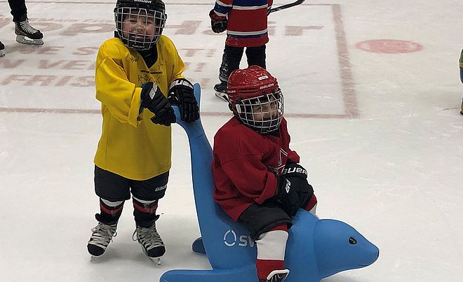Zwei Jungen in Eishockeyausrüstung befinden sich auf der Eisbahn des Curt-Frenzel-Stadions. Einer der beiden sitzt auf einer der neuen swa Eisrobben während der andere sich an dieser festhält.  