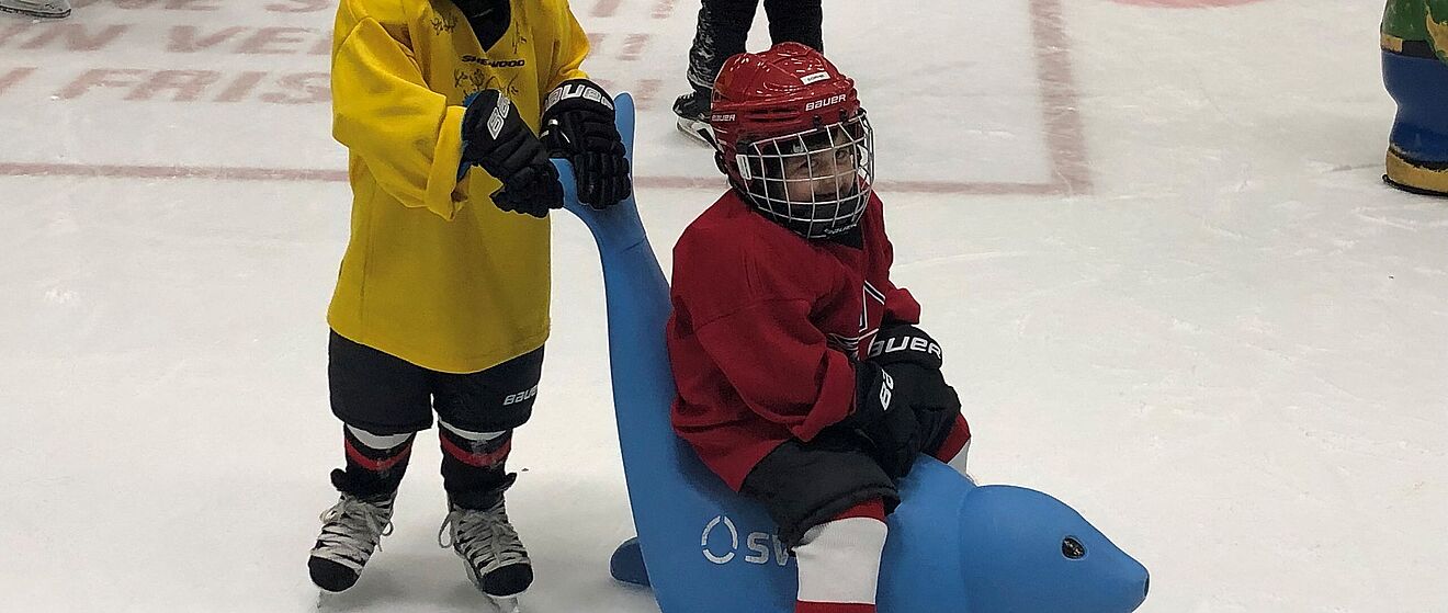 Zwei Jungen in Eishockeyausrüstung befinden sich auf der Eisbahn des Curt-Frenzel-Stadions. Einer der beiden sitzt auf einer der neuen swa Eisrobben während der andere sich an dieser festhält.