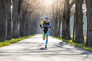Triathlet Lukas Stahl mit swa Kappe läuft auf einem Weg im Wald