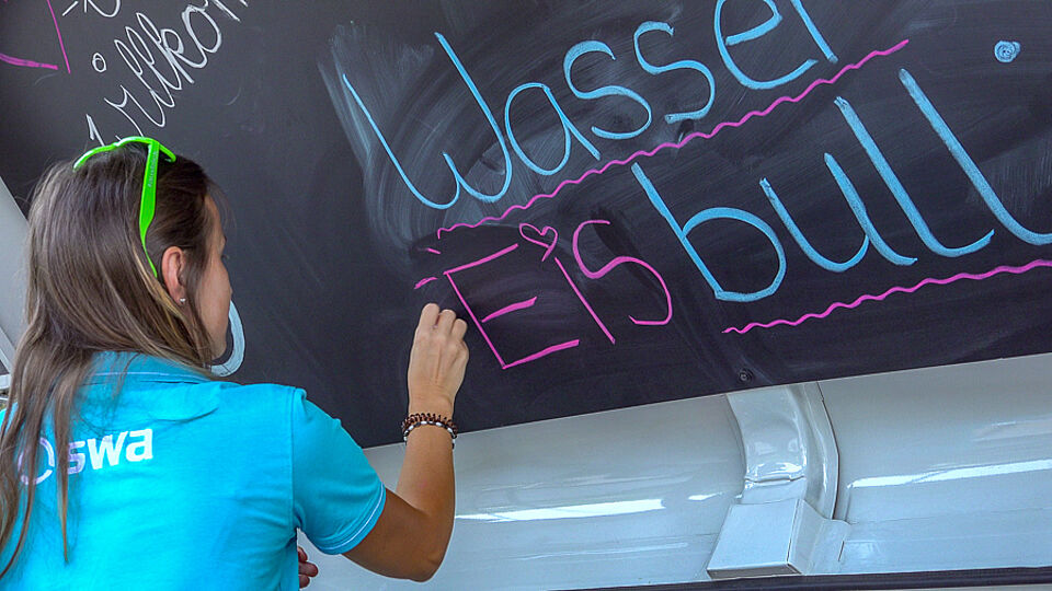 Mädchen schreibt "Wassereis Bulli" auf eine Tafel.