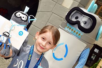 Mädchen steht vor swa Maskottchen Oswald und zeigt Oswald Schlüsselanhänger und Kuscheltier in die Kamera. Ein Klick führt zur Vergrößerung des Bildes.