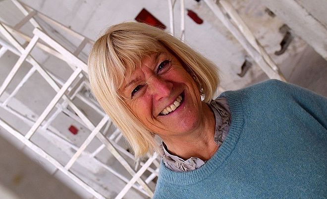 Lachende Frau steht in einem Gebäude vor Skulpturen. Weiterverlinkung auf INTERFERENZEN Newsartikel