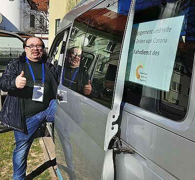 Ein Mann steigt in ein Auto, lächelt in die Kamera und zeigt einen Daumen hoch.