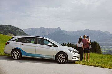 Familie steht neben einem swa Carsharing-Auto. Im Hintergrund ist ein Alpenpanorama.