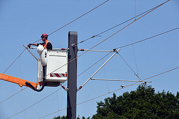 Arbeiter in weißer Hebebühne, an einer Stromleitung vor einem blauen Himmel. - Beim anklicken wird das Bild vergrößert.
