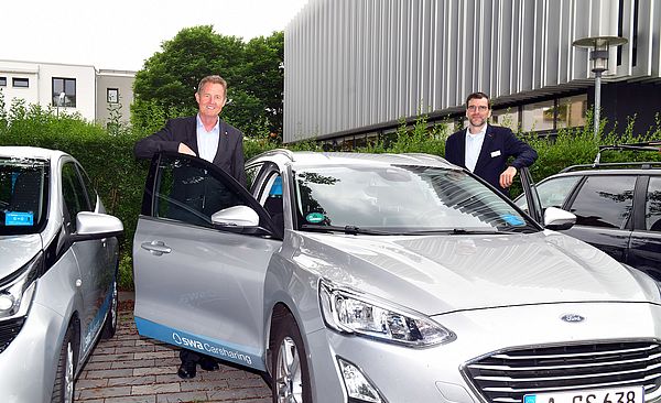 Zwei Männer neben einem swa Carsharing-Auto auf einem Parkplatz