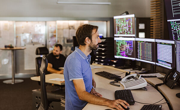 Ein Mann sitzt vor vielen Bildschirmen.